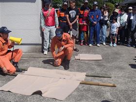 竹棒と毛布で簡易担架の作成方法を学ぶ(川下区))
